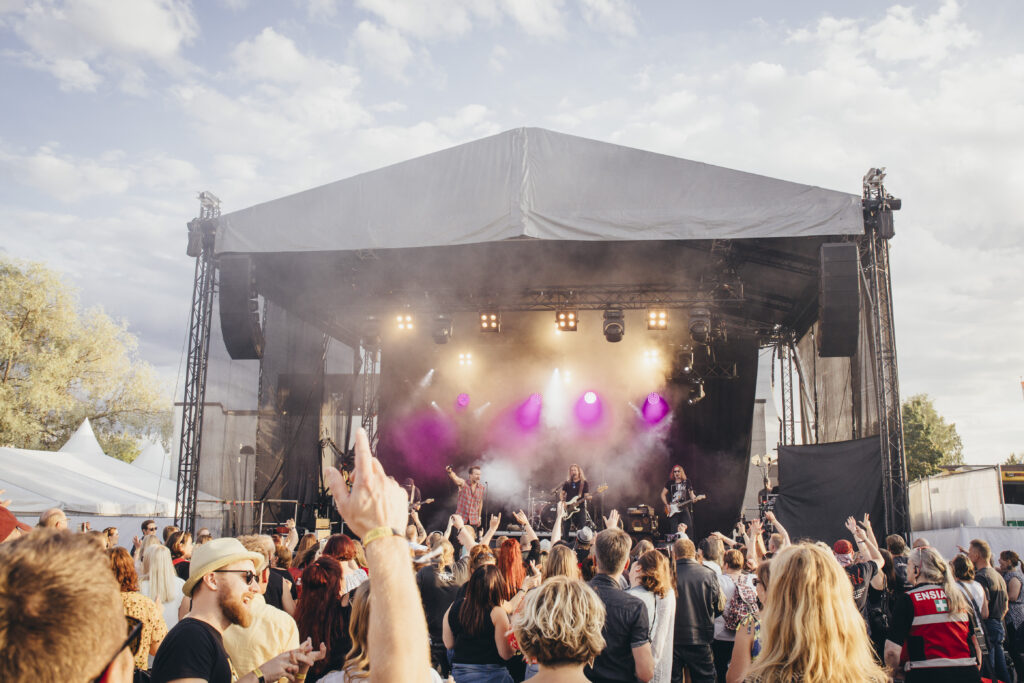 rokkikonsertin lava taustalla etualalla käsiä ja ihmisiä